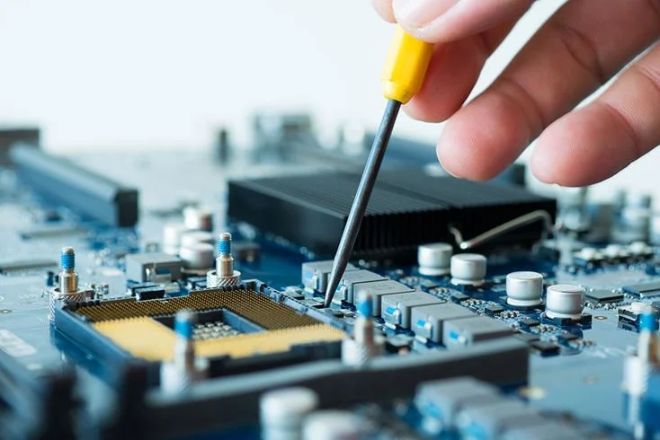 A close-up view of a circuit board with a microcontroller socket, as a hand uses a small screwdriver to adjust or work on electronic components